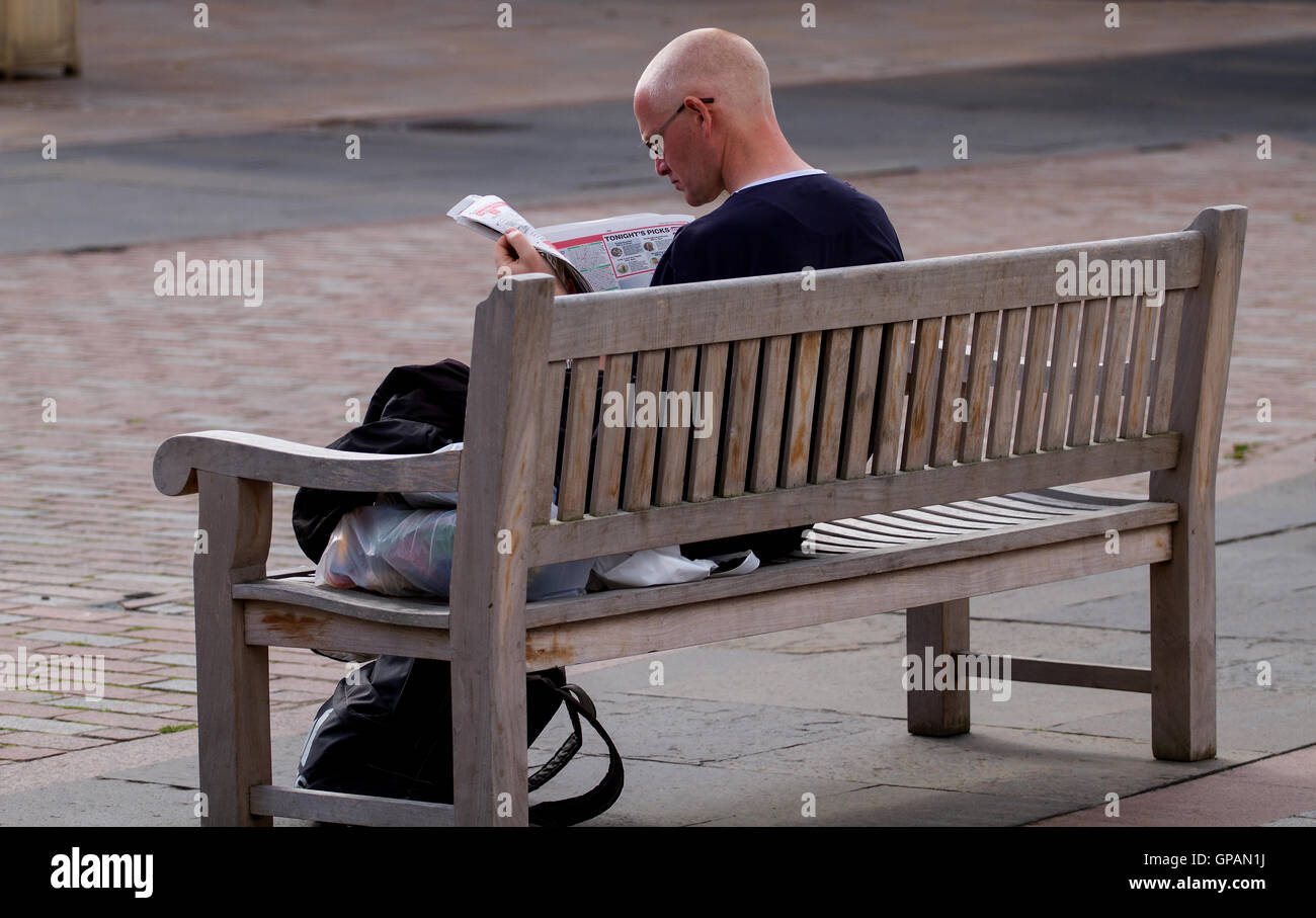 Un homme d'âge moyen assis sur un siège d'été de lire le journal dans le centre de Dundee, Royaume-Uni Banque D'Images