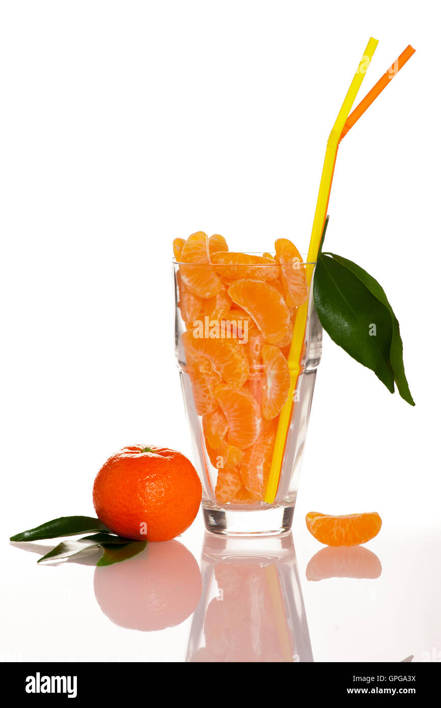 Grand verre rempli de tranches d'agrumes mandarin orange, décoré avec de la paille et des feuilles vertes représentant jus naturel frais Banque D'Images