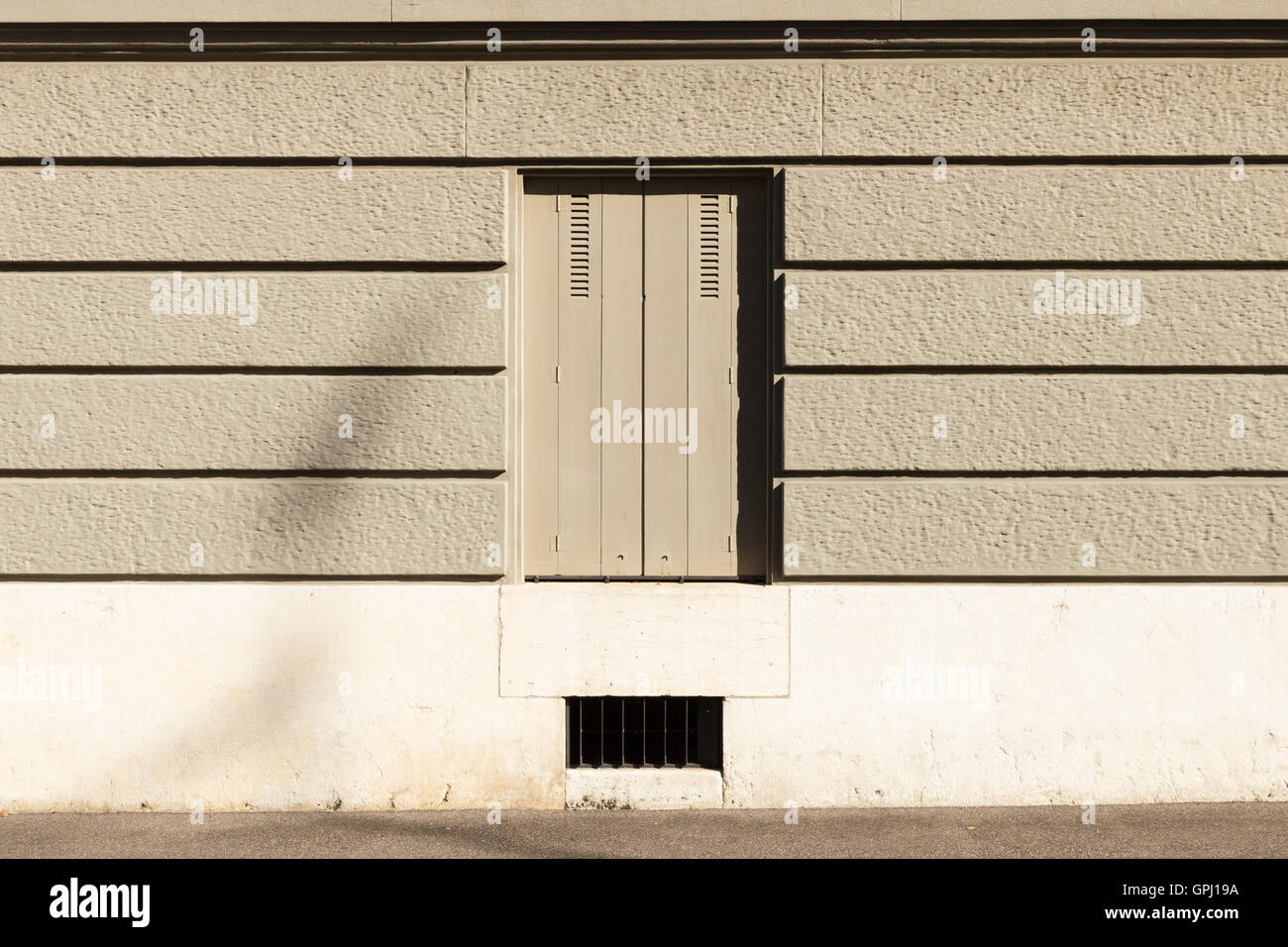 Un mur peint en gris avec des bandes horizontales et une fenêtre avec des volets fermés. Banque D'Images