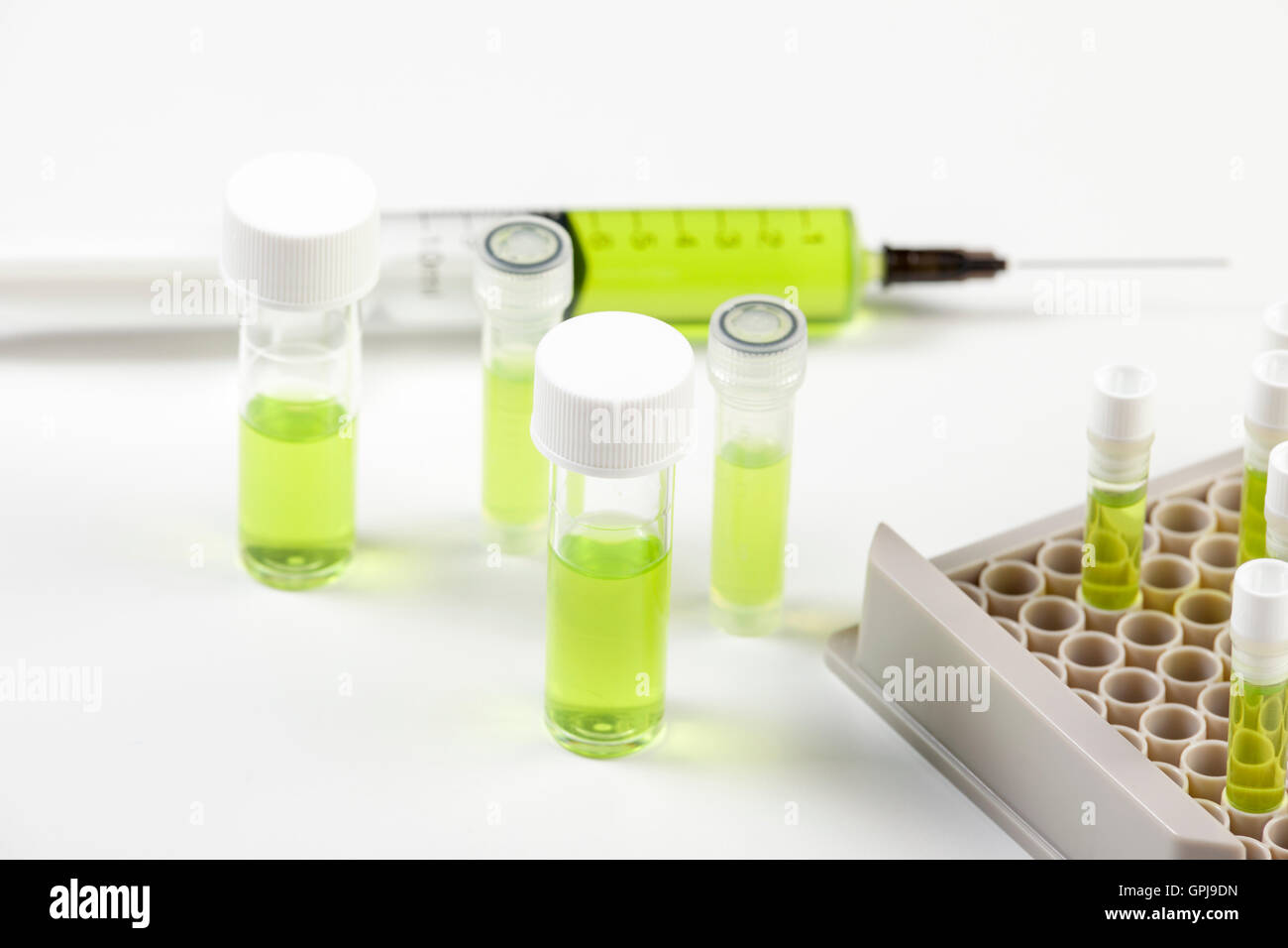 Des fioles fermées et d'une seringue contenant un liquide vert sur fond blanc banc de laboratoire Banque D'Images