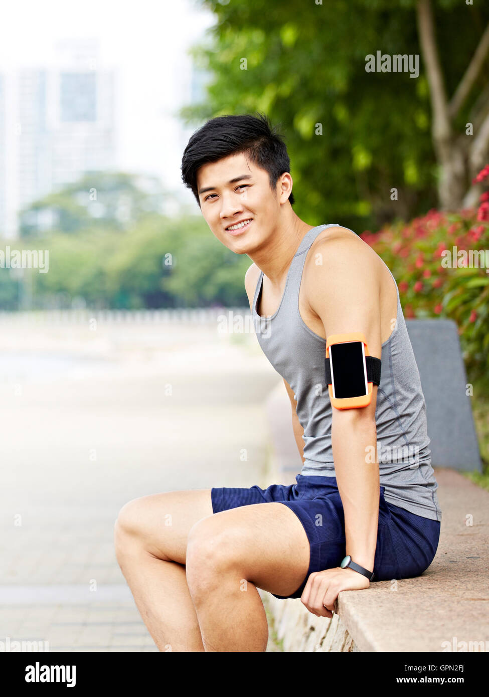 Les jeunes bel asiatique jogger port tracker remise en forme en faisant une pause dans un parc de la ville, avec un grand sourire Banque D'Images
