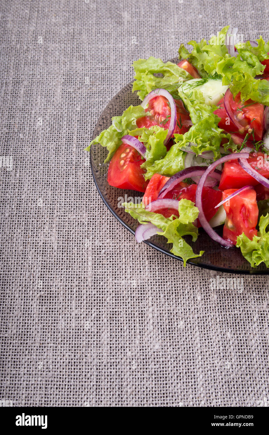 Fragment d'une plaque transparente avec une salade de légumes crus sur un gros plan de table tapis gris Banque D'Images