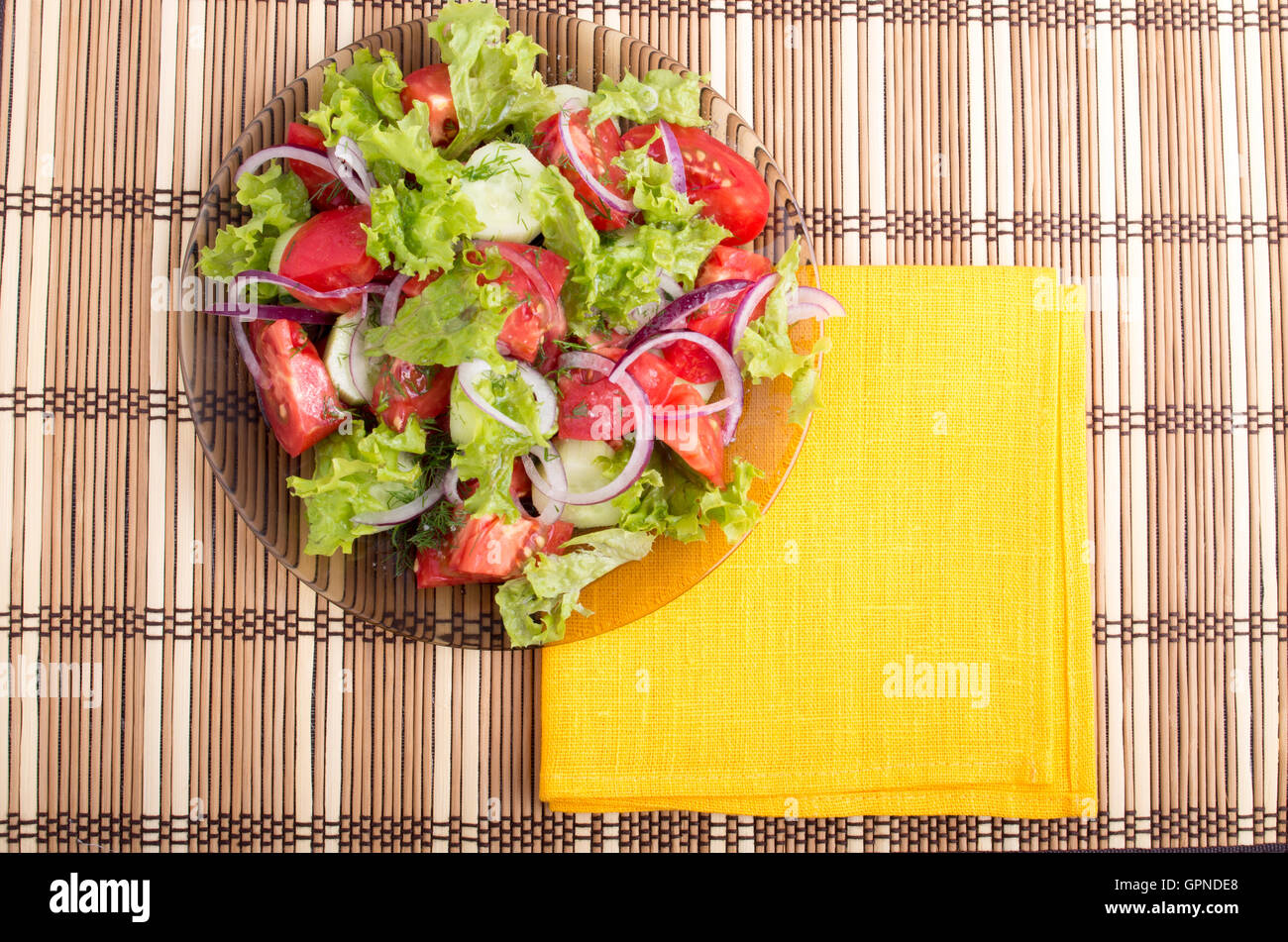 Plaque transparente avec salade d'été frais et une serviette jaune vif sur une table recouverte d'un tapis de bambou Banque D'Images
