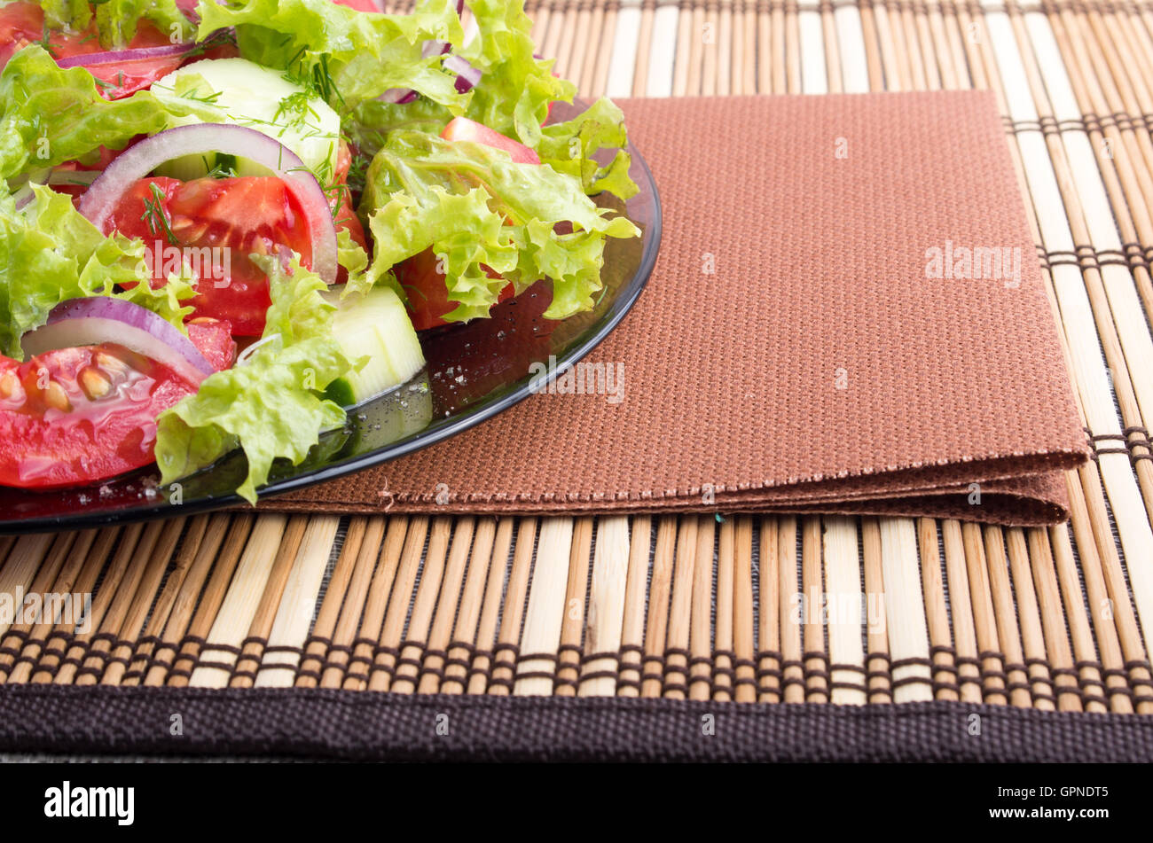 Fond Foodstyle vue rapprochée d'une plaque avec une salade fraîche de tomates crues et de laitue et brown serviette sur un tapis de bambou Banque D'Images