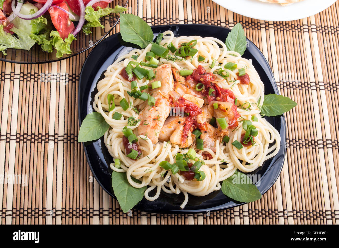 Ragoût de poulet avec sauce de tomate sur une assiette avec des spaghetti décorée de feuilles de basilic et oignons sur la table à manger est couvert Banque D'Images