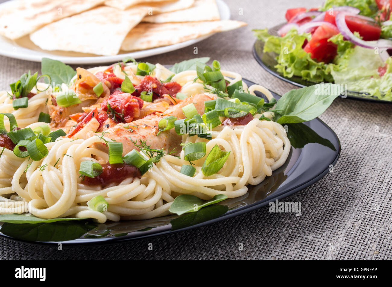 Libre de la plaque noire avec des spaghetti et des morceaux de poulet compote décoré de feuilles de basilic et oignons est à la table de dîner wi Banque D'Images