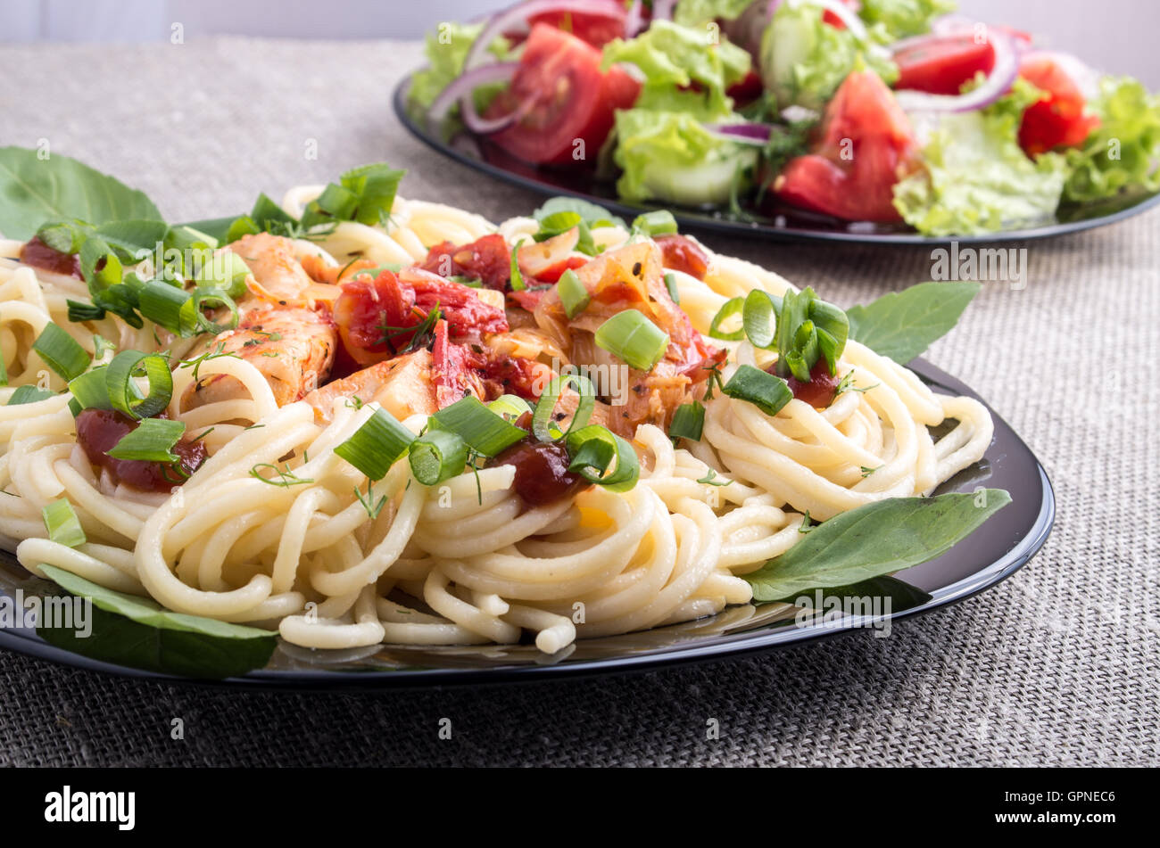 Des repas faits maison sur un tapis gris - spaghetti avec des morceaux de poulet et de légumes à l'étuvée avec salade de tomate et laitue Banque D'Images