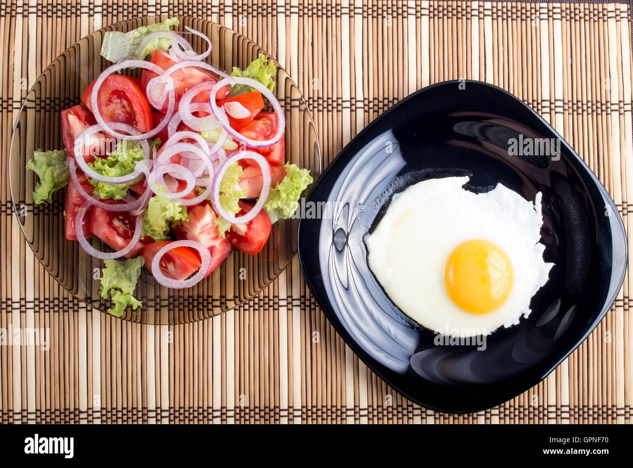 Vue de dessus sur un œuf frit sur une plaque noire et une salade de tomate, de laitue et d'oignon sur un tapis à rayures Banque D'Images