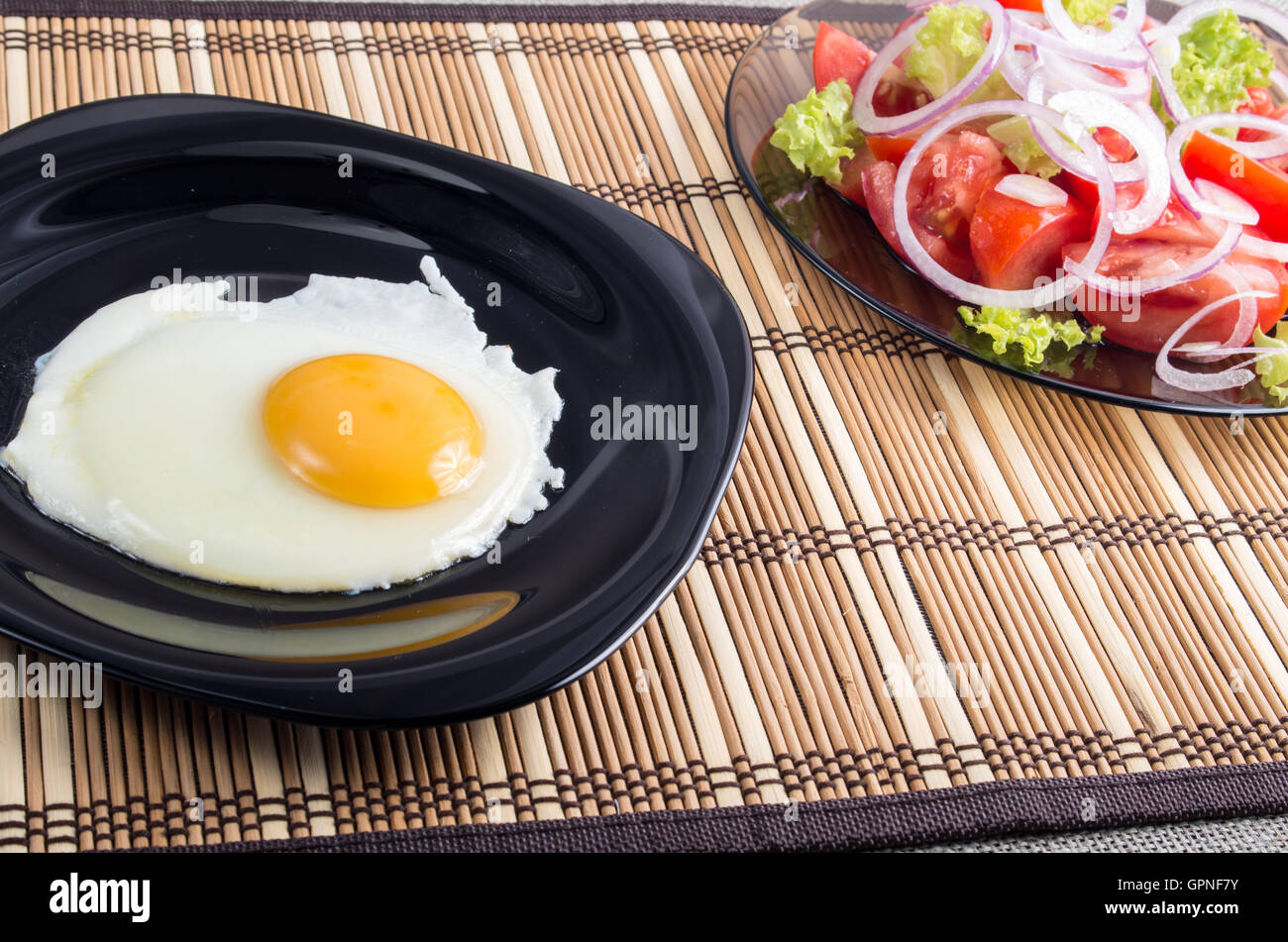 Vue rapprochée sur les petit-déjeuner fait maison d'œuf frit et salade de tomates fraîches sur un tapis à rayures Banque D'Images