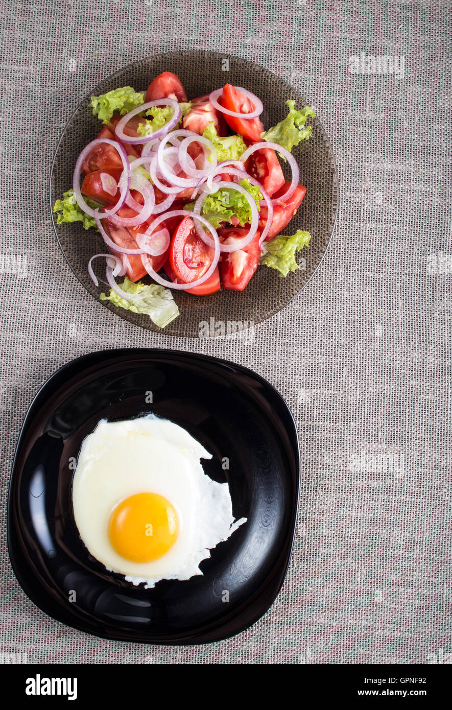 Vue de dessus d'un petit-déjeuner maison saine d'œufs sur le plat et une salade de tomates hachées dans une assiette sur la table d'examen Banque D'Images