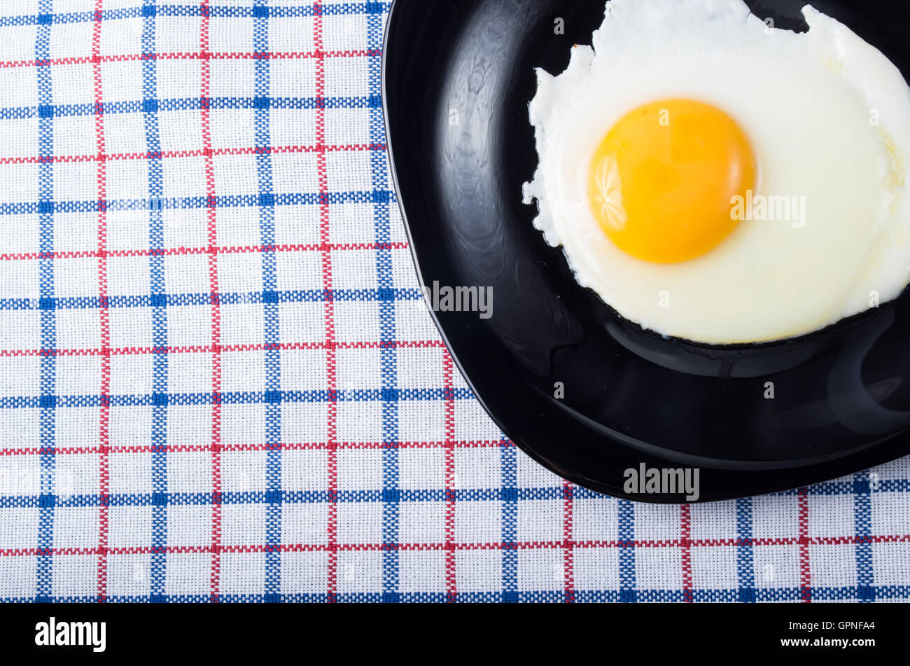 Vue de dessus sur une plaque noire avec un œuf frit avec un oeuf sur une table couverte d'une nappe libre Banque D'Images