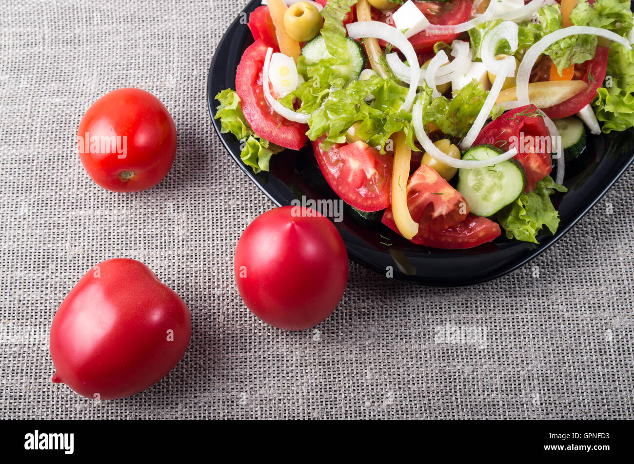 Vue de dessus Gros plan sur la tomate fraîche et une partie d'une assiette avec la salade végétarienne sur une table recouverte d'un tapis gris Banque D'Images