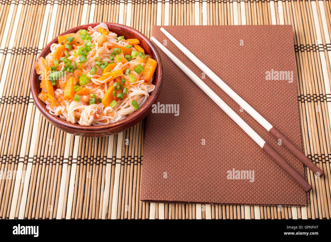 Vue de dessus d'un bol de nouilles de riz asiatiques et condiments dans un petit bol en bois sur un tapis à rayures Banque D'Images