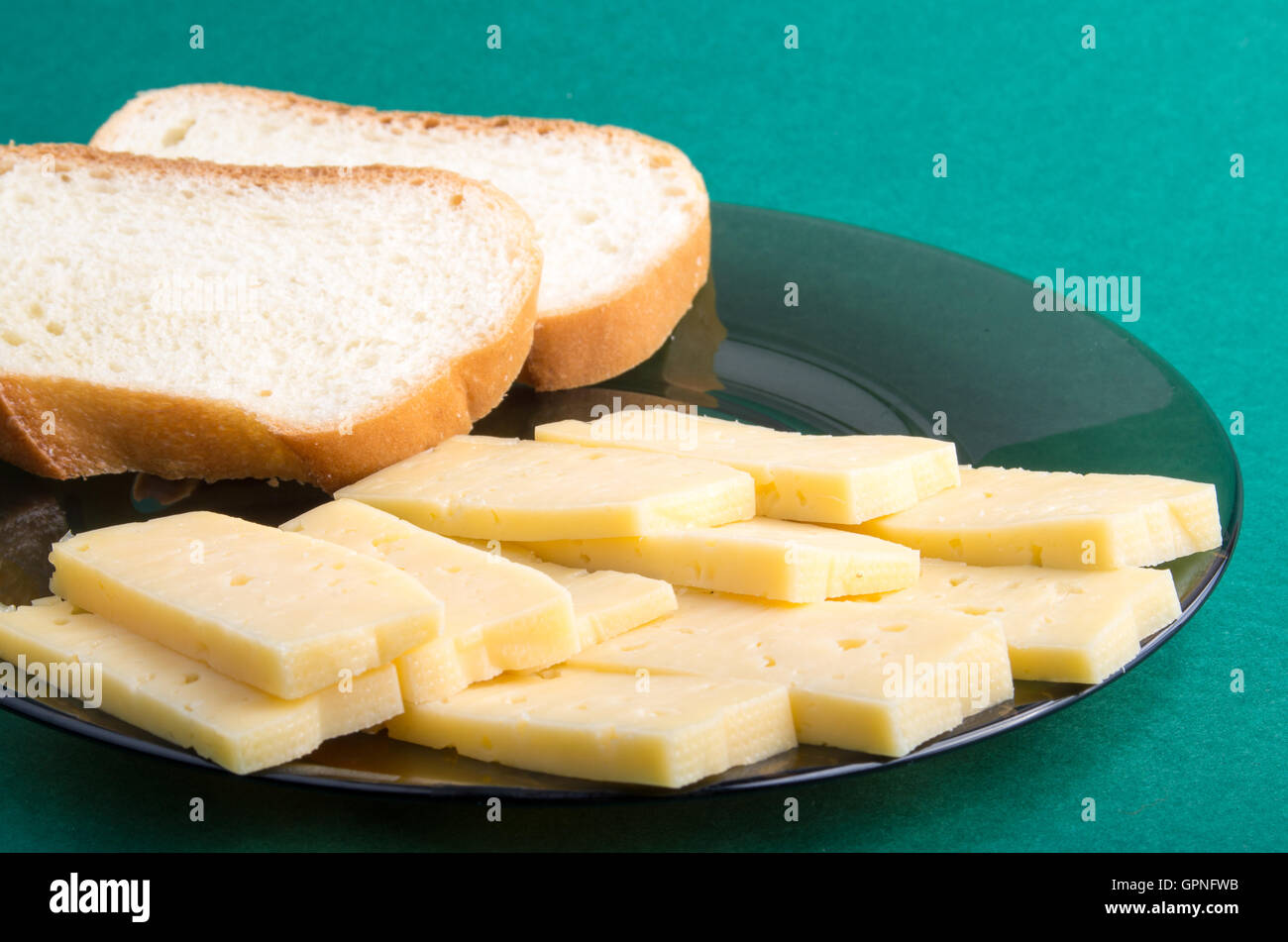 Plaque sur fond vert jaune avec des tranches de fromage et des morceaux de pain blanc libre Banque D'Images