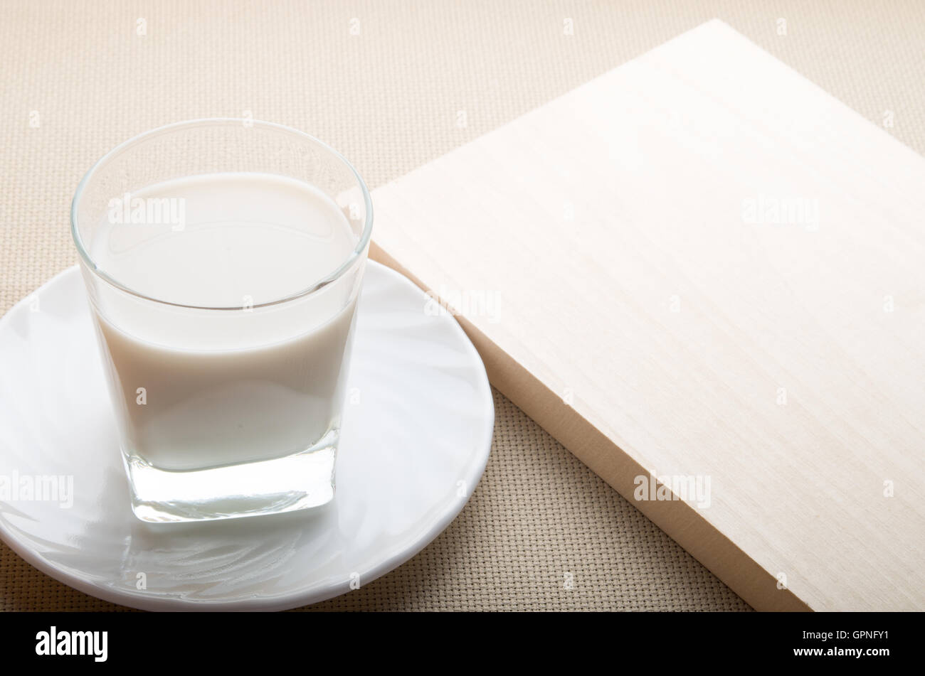 Un verre de lait sur une soucoupe blanc avec un bord en bois naturel sur fond nappe Banque D'Images