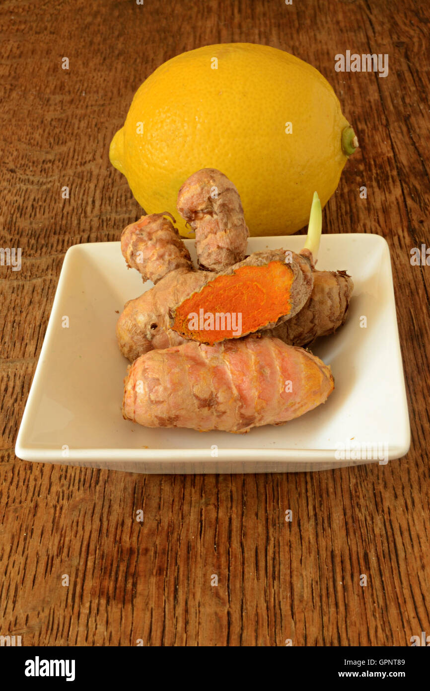 Racine de curcuma & citron allongé sur la table en bois sombre. L'une des racines est tranché et a commencé à germer. Le curcuma est un tonique naturel Banque D'Images