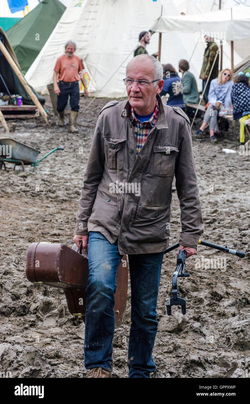 Un festival-goer transportant une guitare trudges dans la boue au festival de Glastonbury Banque D'Images