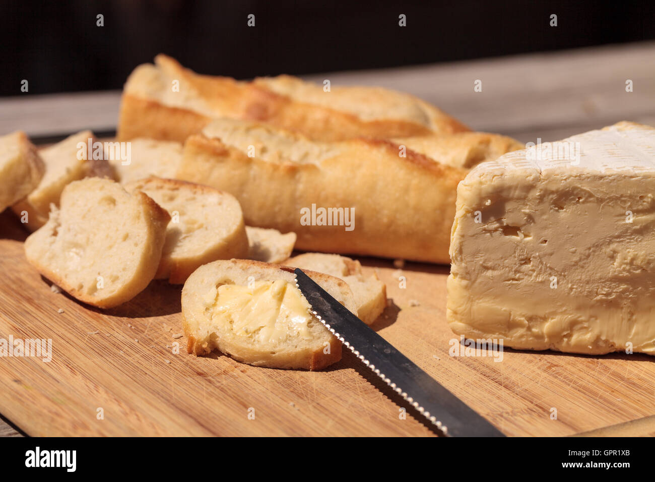 Pain français et fromage brie triple crème sur une planche à découper avec un couteau. Banque D'Images