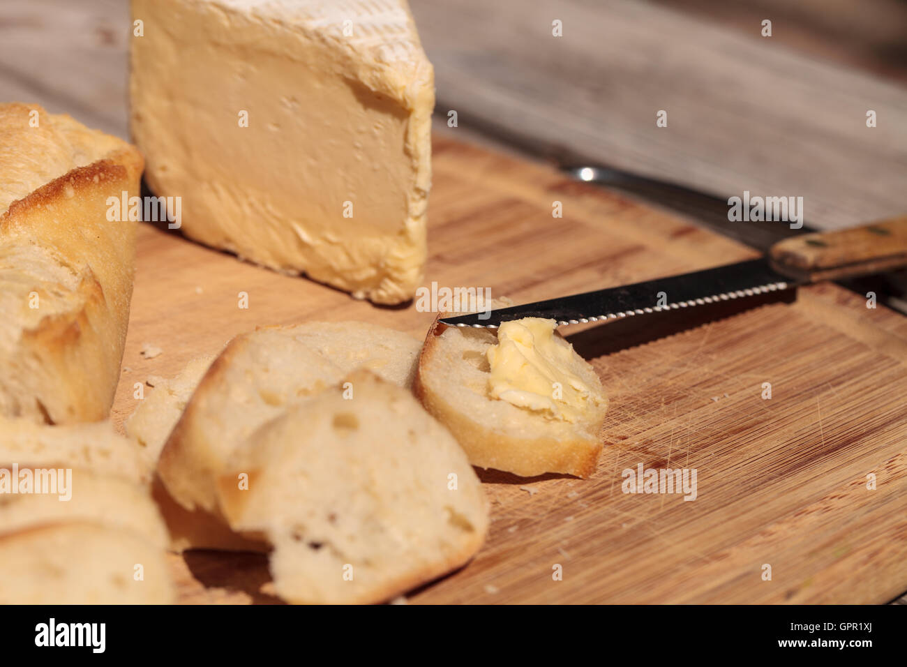 Pain français et fromage brie triple crème sur une planche à découper avec un couteau. Banque D'Images