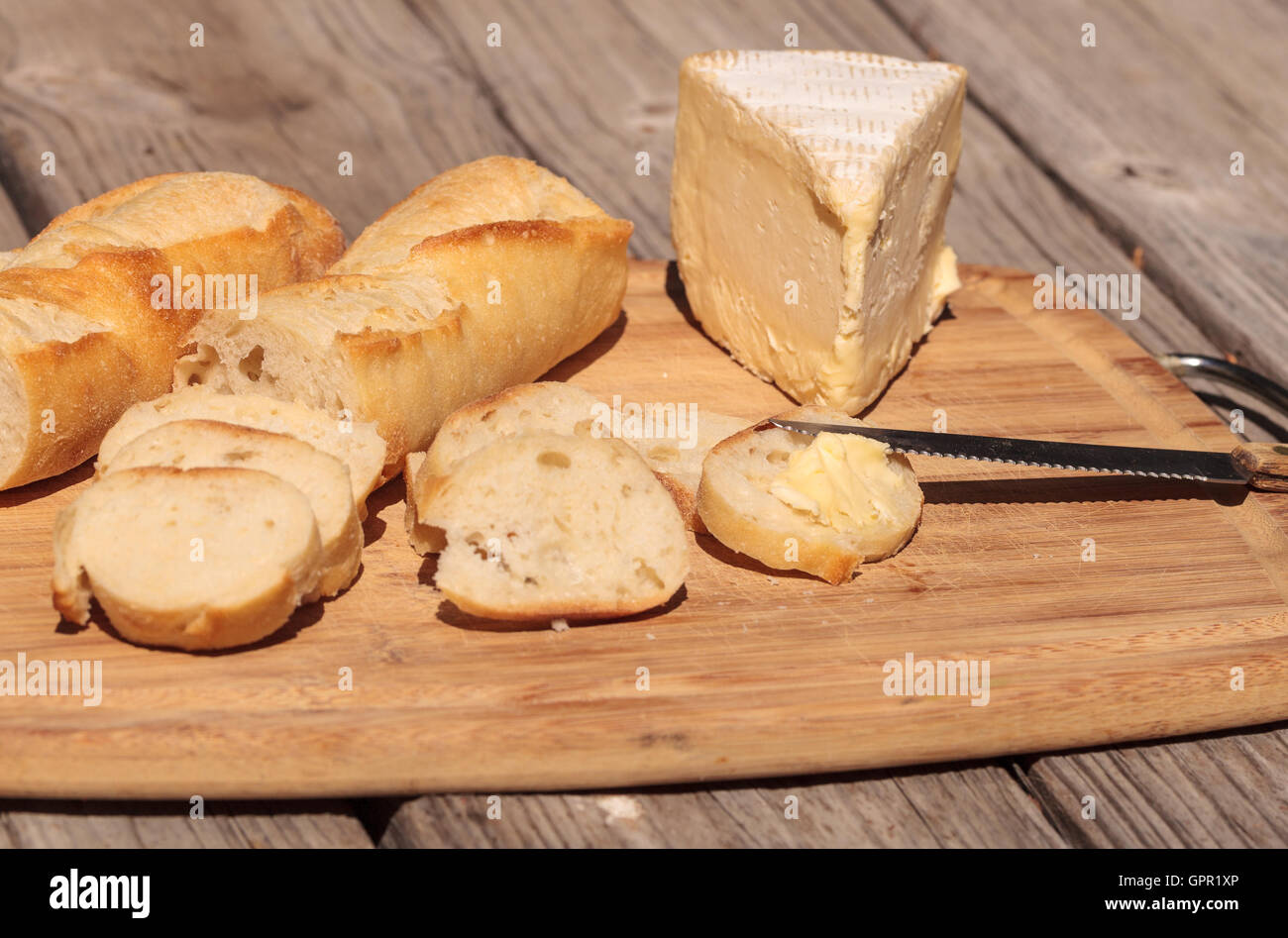 Pain français et fromage brie triple crème sur une planche à découper avec un couteau. Banque D'Images