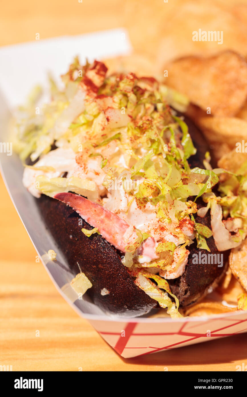 Rouleau de homard du Maine gastronomique sur un petit pain de seigle et de pommes de terre frites à la plage en été. Banque D'Images