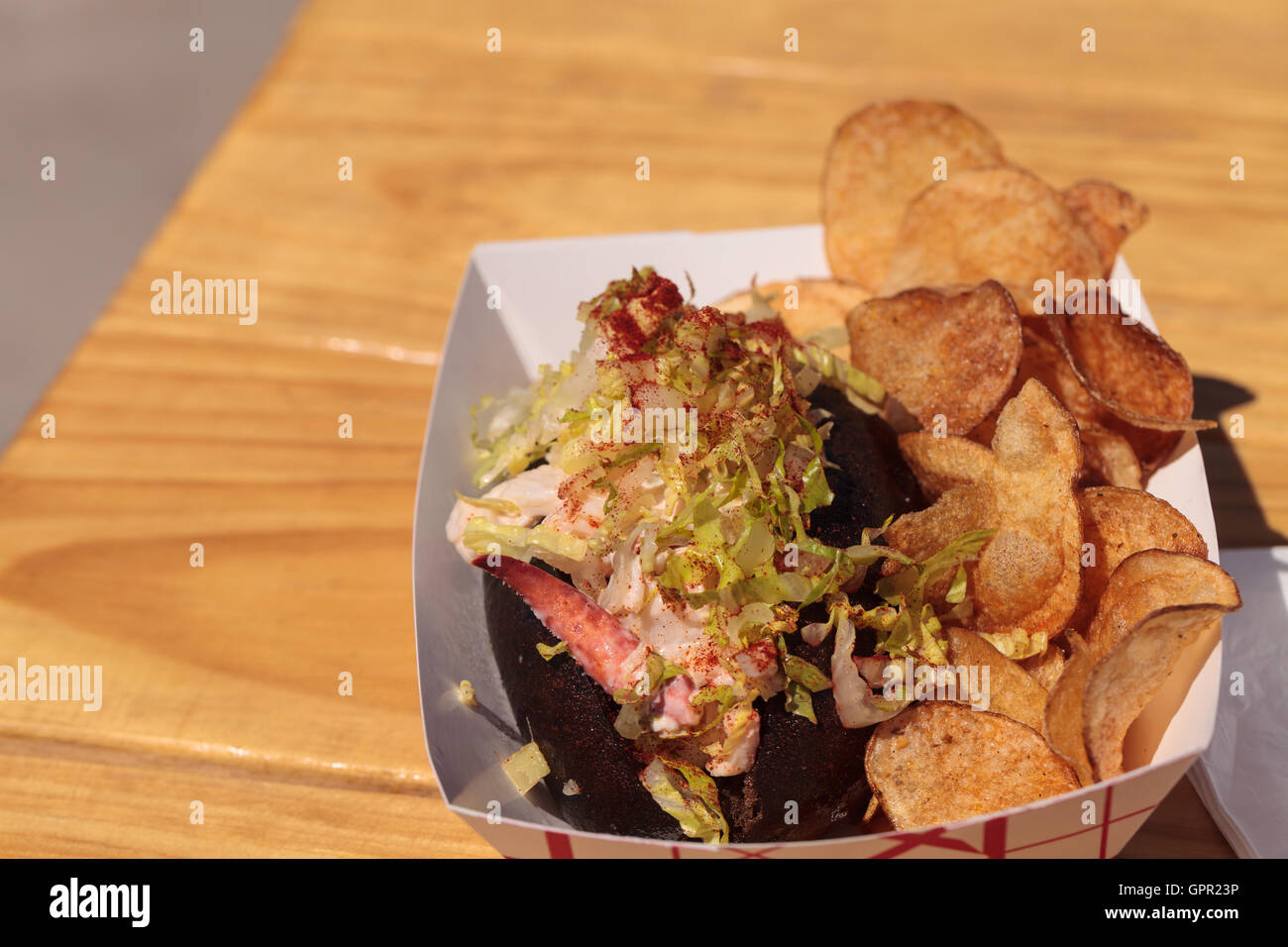 Rouleau de homard du Maine gastronomique sur un petit pain de seigle et de pommes de terre frites à la plage en été. Banque D'Images