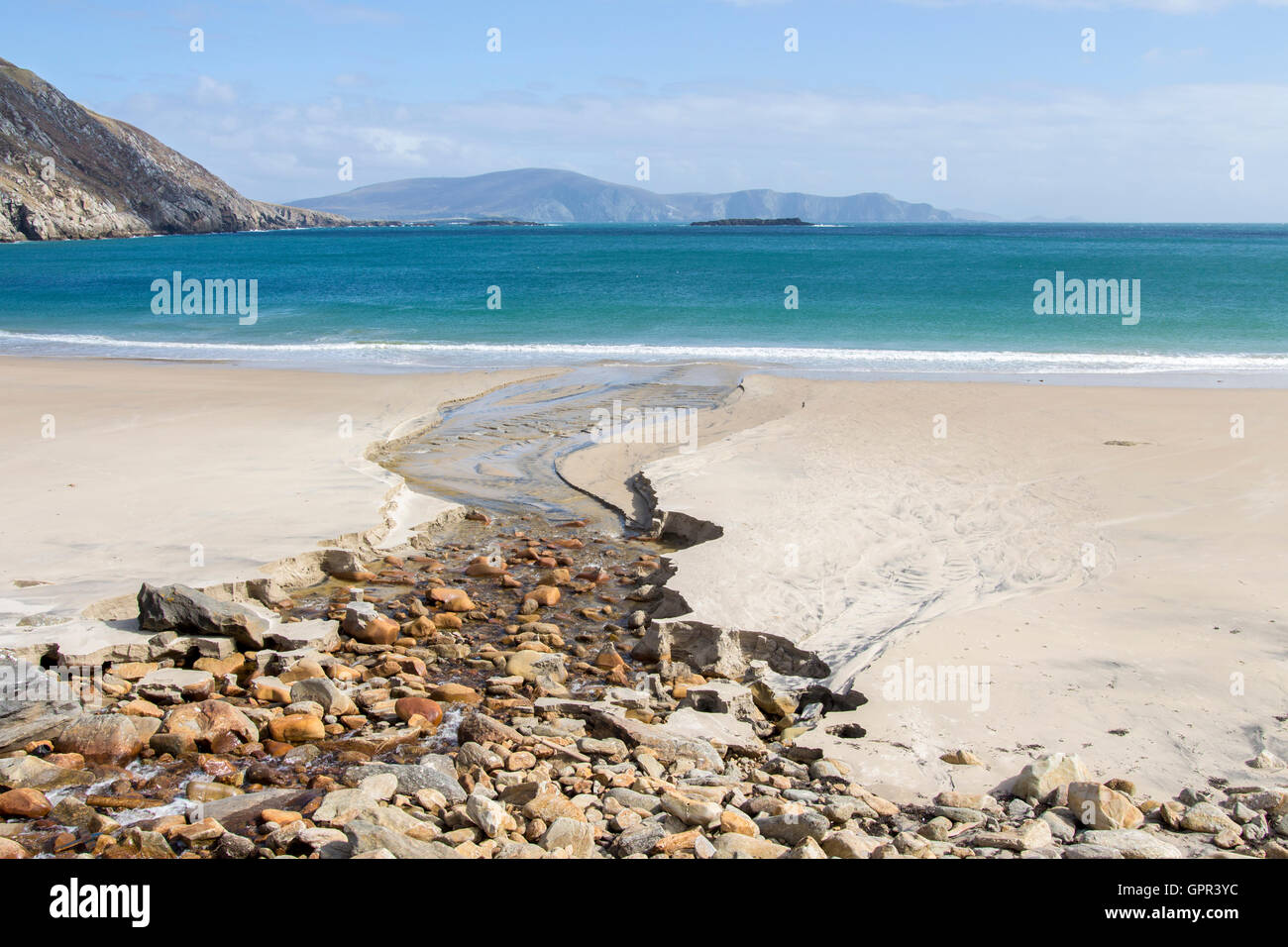 Un petit ruisseau mène l'oeil par une plage de sable fin de belles eaux turquoise sur une journée ensoleillée et claire pour la plupart. Banque D'Images