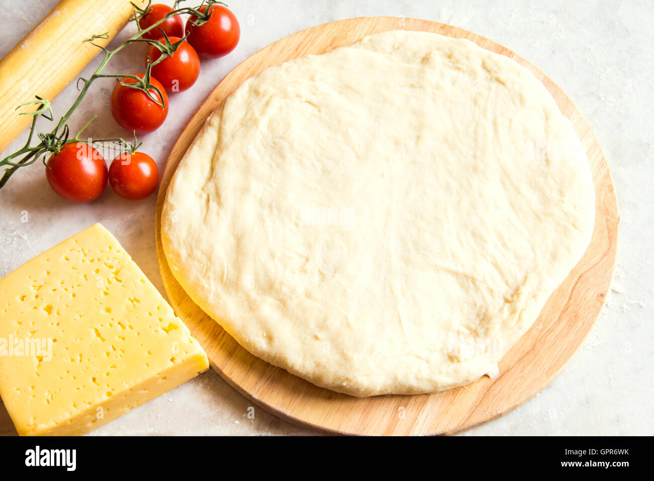 La pâte sur une planche à découper, tomates et fromage pour pizza sur tableau blanc Banque D'Images