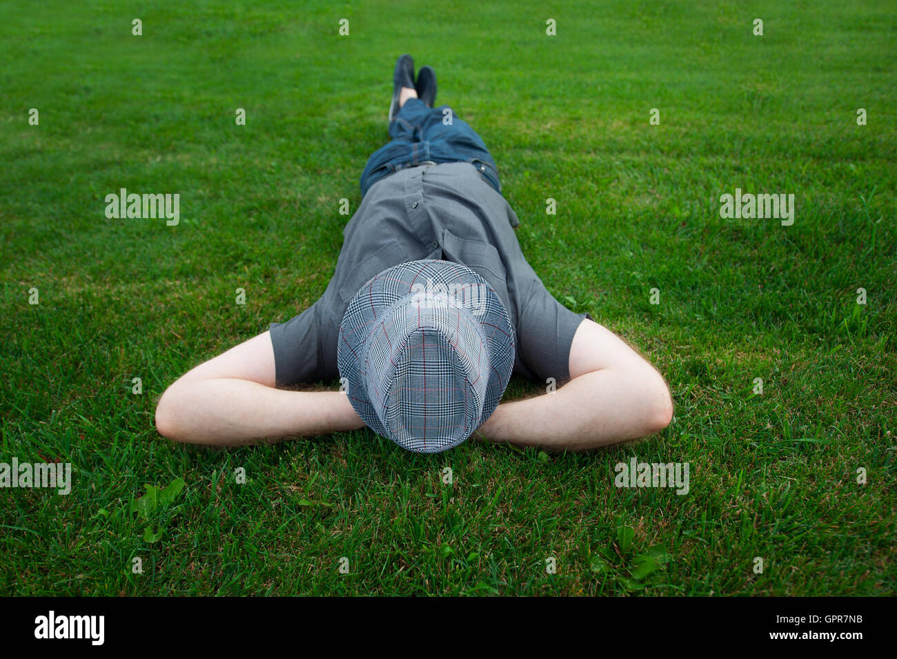 Homme étendu dans un champ sur l'herbe verte avec le chapeau sur son visage Banque D'Images