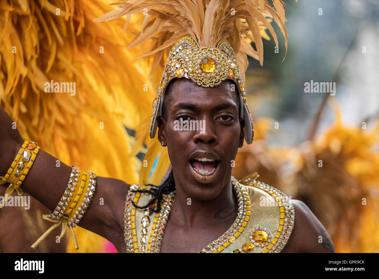 Homme noir Afro Antillais en costume avec une coiffure de plumes jaunes au carnaval de Notting Hill dans l'ouest de Londres Banque D'Images