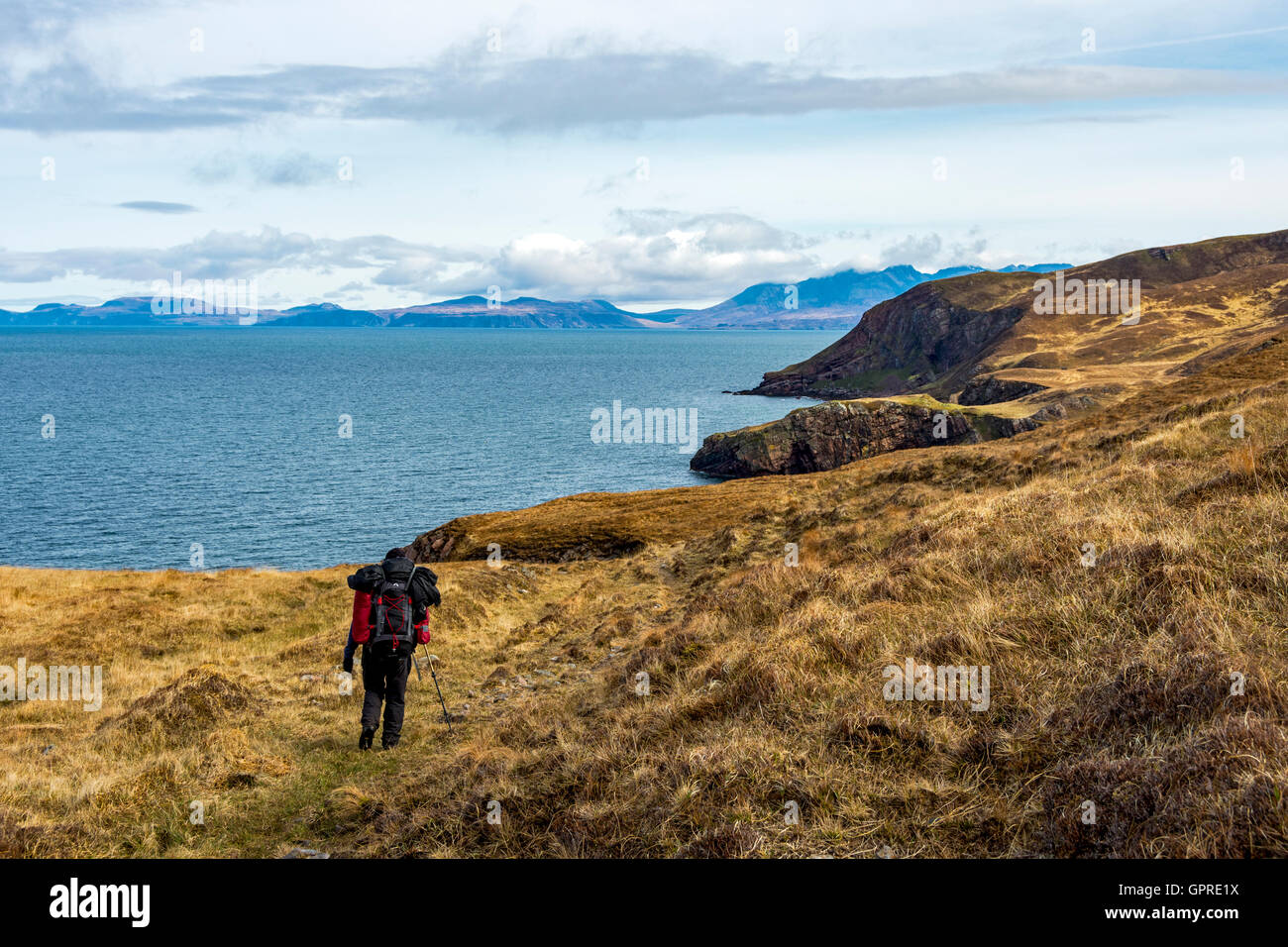 Un marcheur sur la piste côtière de Guirdil Shellesder Glen Bay à l'île de Skye, dans la distance, à l'île de Rum, Ecosse, Royaume-Uni. Banque D'Images