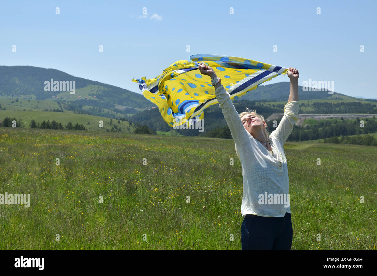 Femme tenant l'écharpe jaune et bleu qui est sur le vent agitant en paysage Banque D'Images