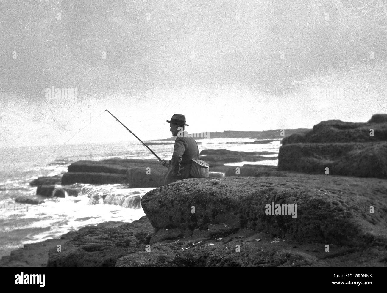 Années 1930, historiques, Sidney H.Smith assis sur les roches du littoral à marée basse de pêche à Filey Brigg, un promontoire, North Yorkshire, Angleterre. Banque D'Images