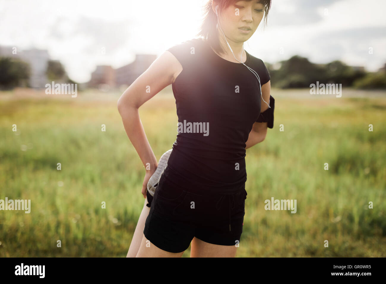 Tourné d'une jeune femme qui s'étend les jambes. Femme d'origine asiatique dans les vêtements de sport faisant réchauffer l'exercice dans les matins dans un parc. Banque D'Images