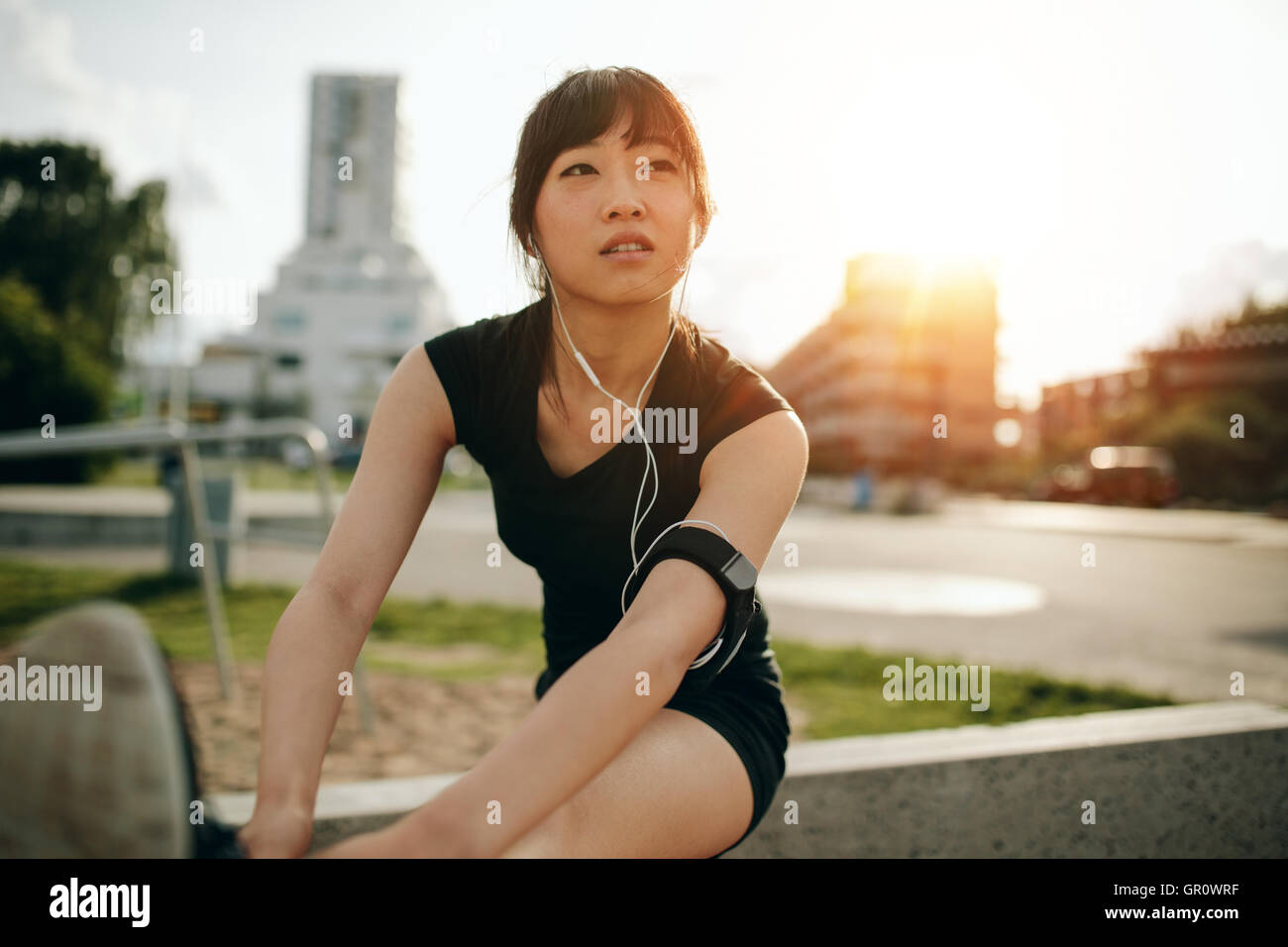 Fit woman stretching ses jambes avant une séance de formation. Bel athlète chinois exerçant à l'extérieur dans le parc de la ville. Banque D'Images
