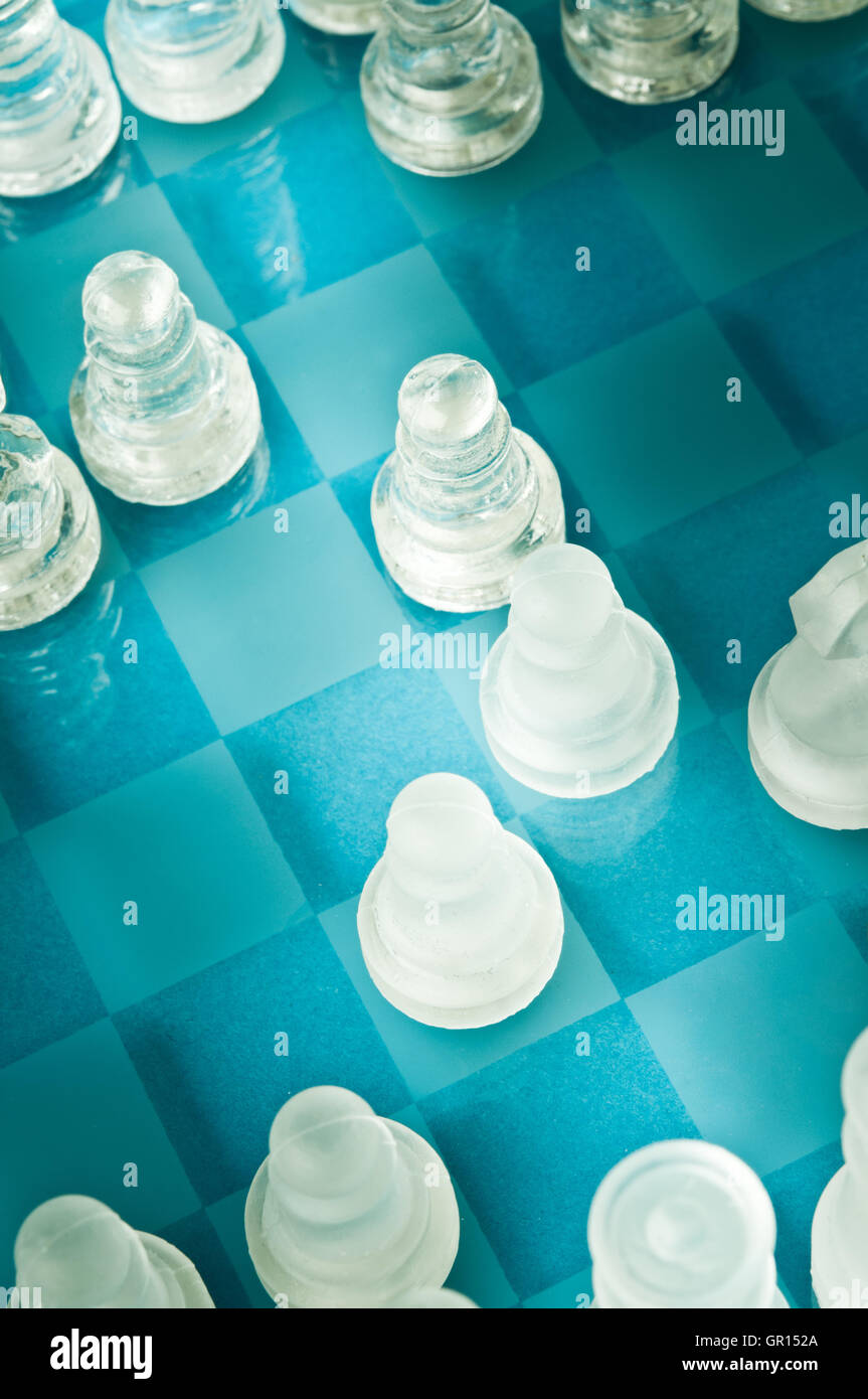 Gros plan de pièces d'échecs en verre mat et transparent sur un échiquier en verre bleu, vu de dessus sous un angle diagonal Banque D'Images