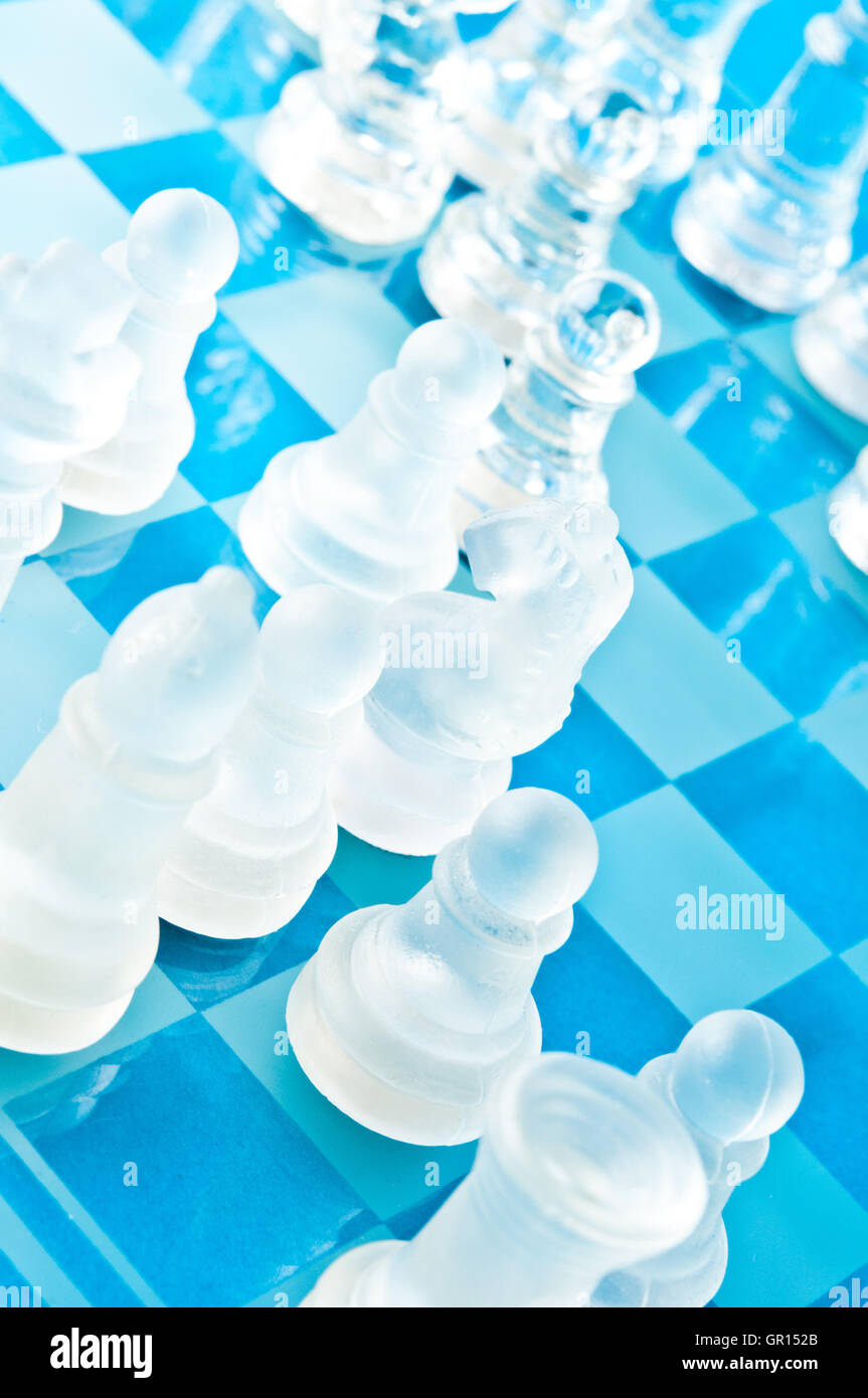 Gros plan de pièces d'échecs en verre mat et transparent sur un échiquier en verre bleu, vu de dessus sous un angle diagonal Banque D'Images