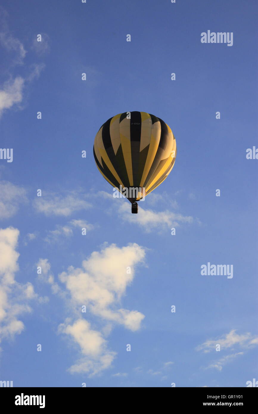 Hot Air Balloon, jaune et noir, vol montgolfier contre ciel bleu nuages blancs Banque D'Images