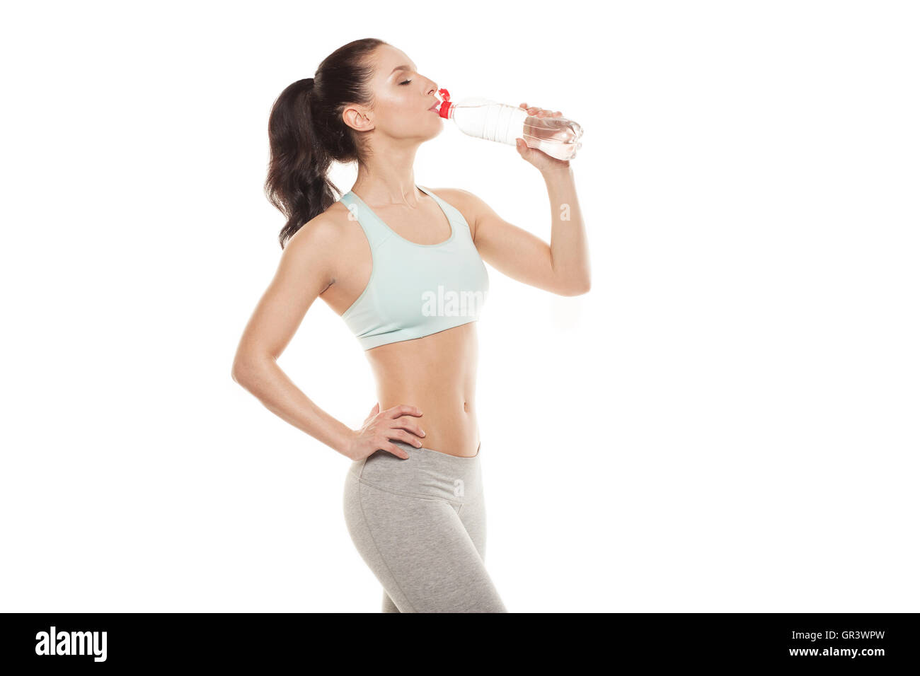 Fille sportive l'eau potable à partir d'une bouteille après un entraînement, entraînement physique, isolé sur fond blanc Banque D'Images