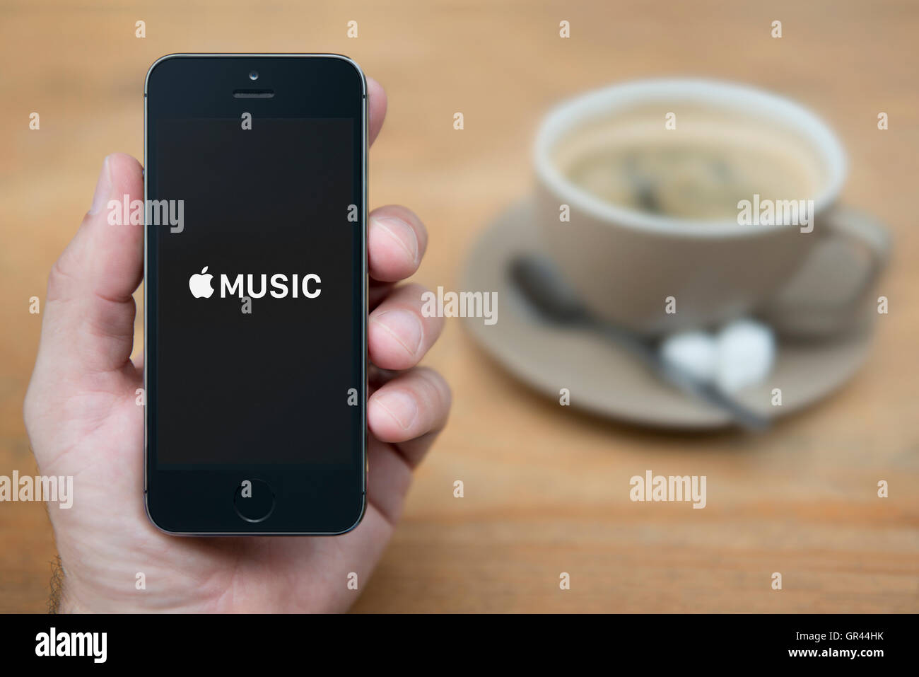 Un homme se penche sur son iPhone qui affiche le logo Apple Musique, tandis que sam avec une tasse de café (usage éditorial uniquement). Banque D'Images