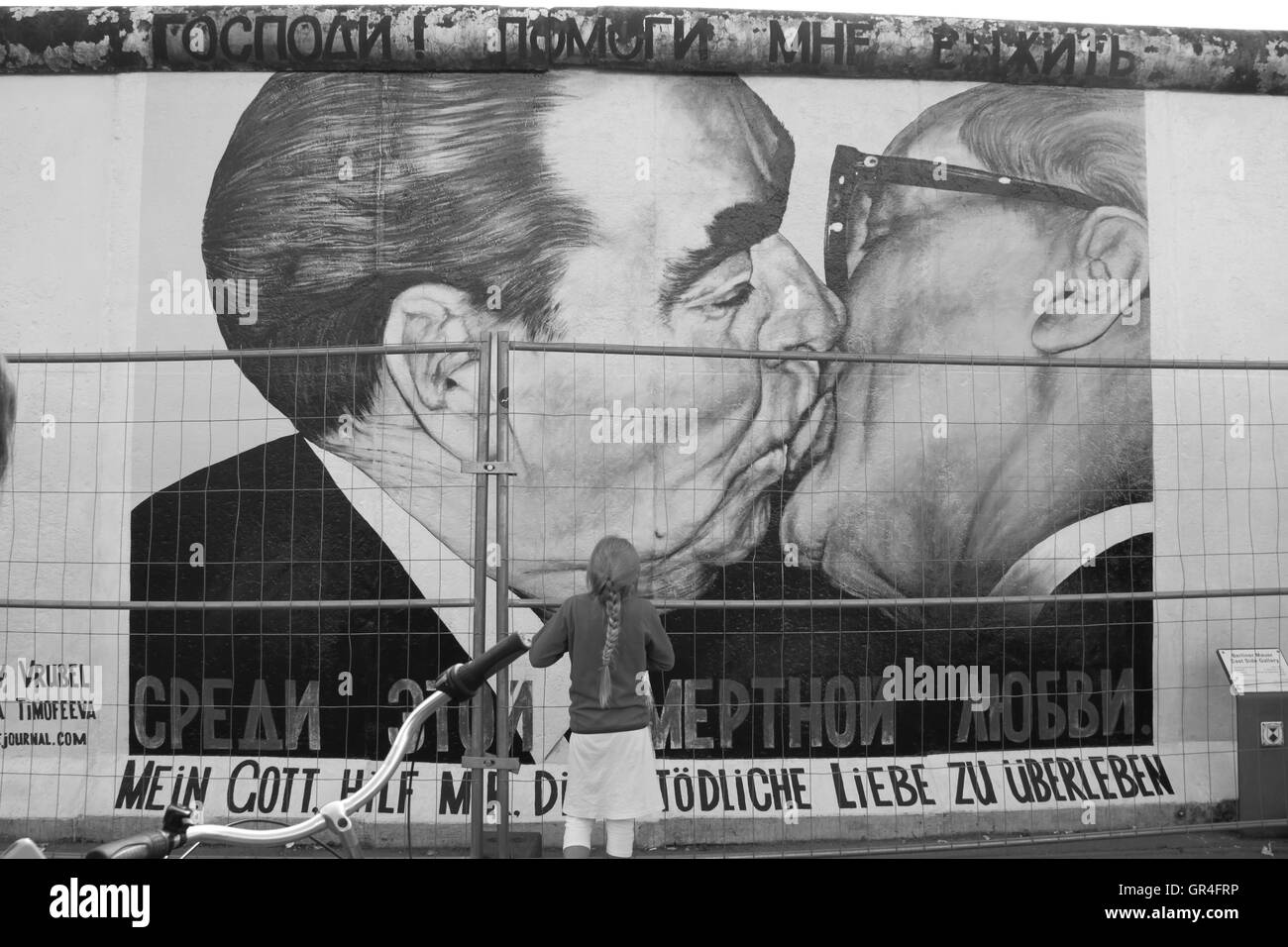 Une fille qui regarde fixement le graffiti de baisers sur le mur de Berlin. Banque D'Images