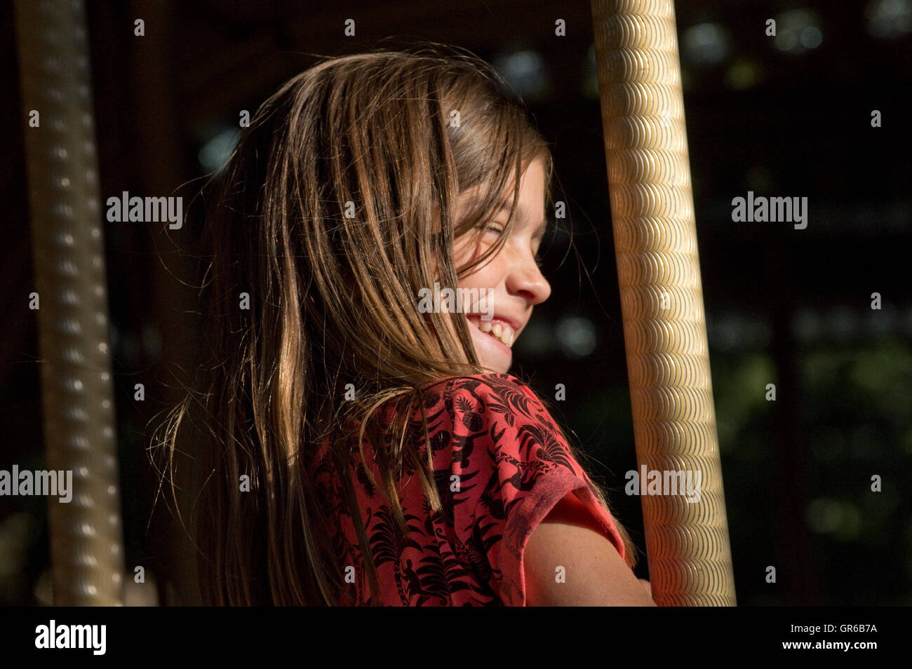 Jeune fille pris dans la lumière du soleil et souriant, assis sur un cheval sur un champ de foire merry go round Banque D'Images