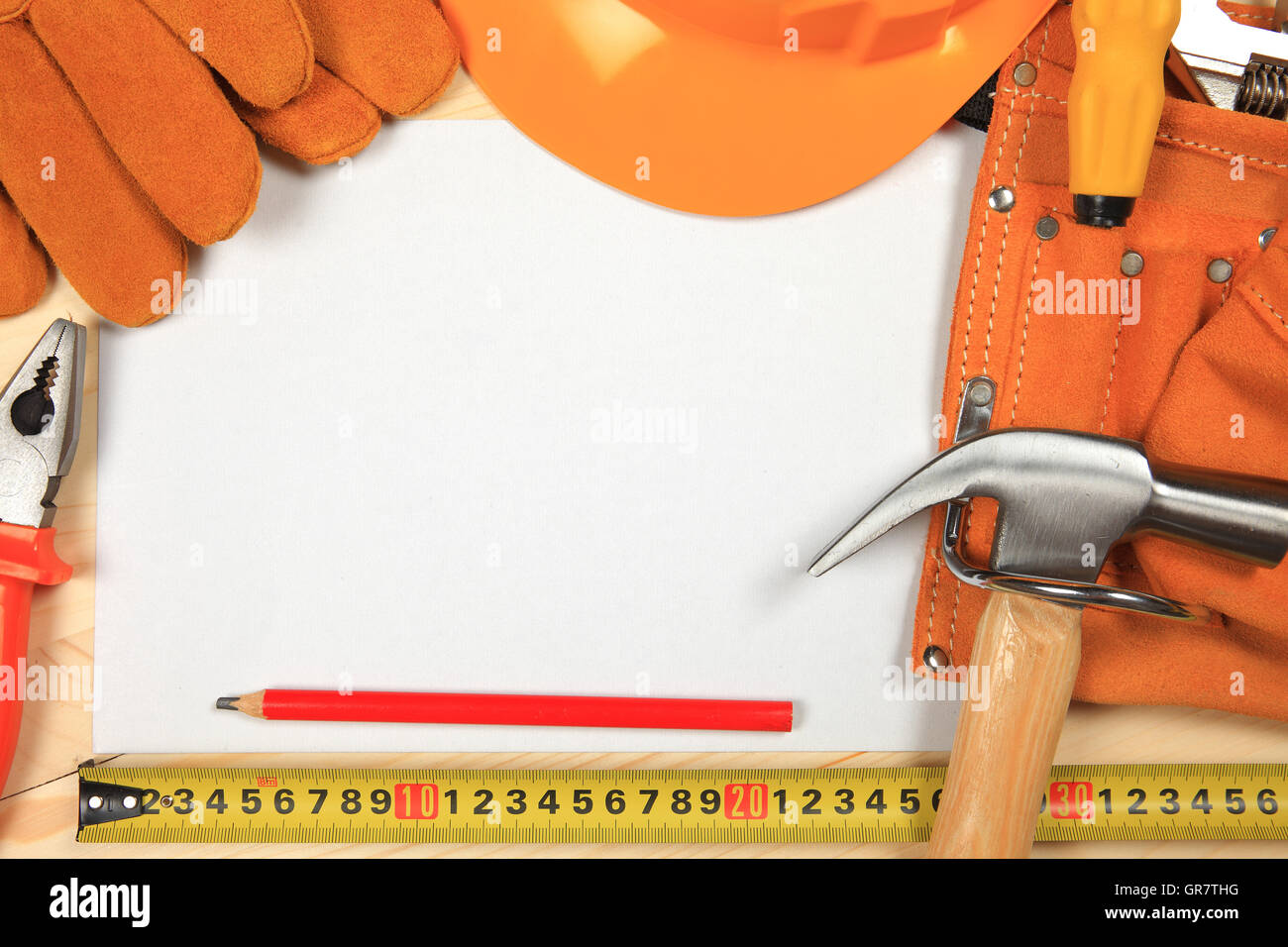 Hard Hat, marteau, pinces, clous, crayon rouge, gants de travail et d'autres outils isolé sur un fond de bois avec une feuille de p Banque D'Images