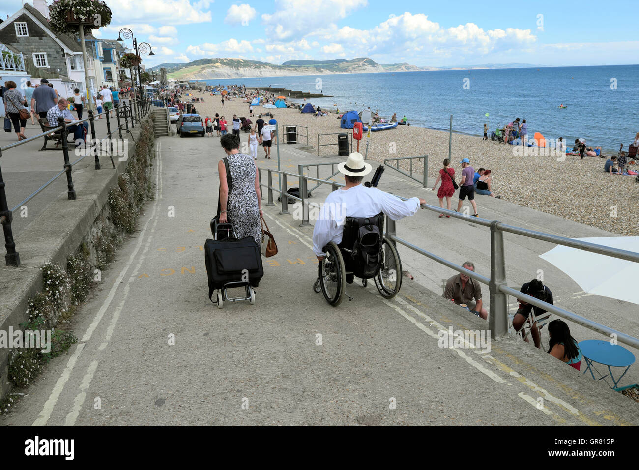 Voyageurs handicapés en fauteuil roulant dans l'homme de descendre une rampe pour la promenade et la plage ville côtière, Lyme Regis, dans le Dorset, Angleterre Royaume-uni Grande-bretagne KATHY DEWITT Banque D'Images