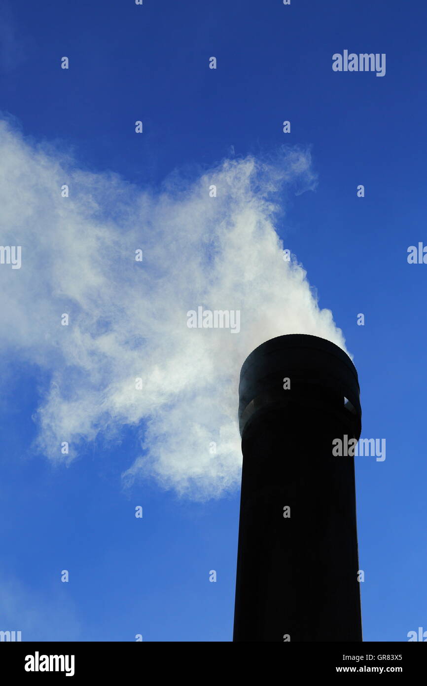 Déverse de fumée d'une cheminée sous un ciel bleu clair dynamique. Les émissions de CO2 sont élevés sur les préoccupations concernant le changement climatique Banque D'Images