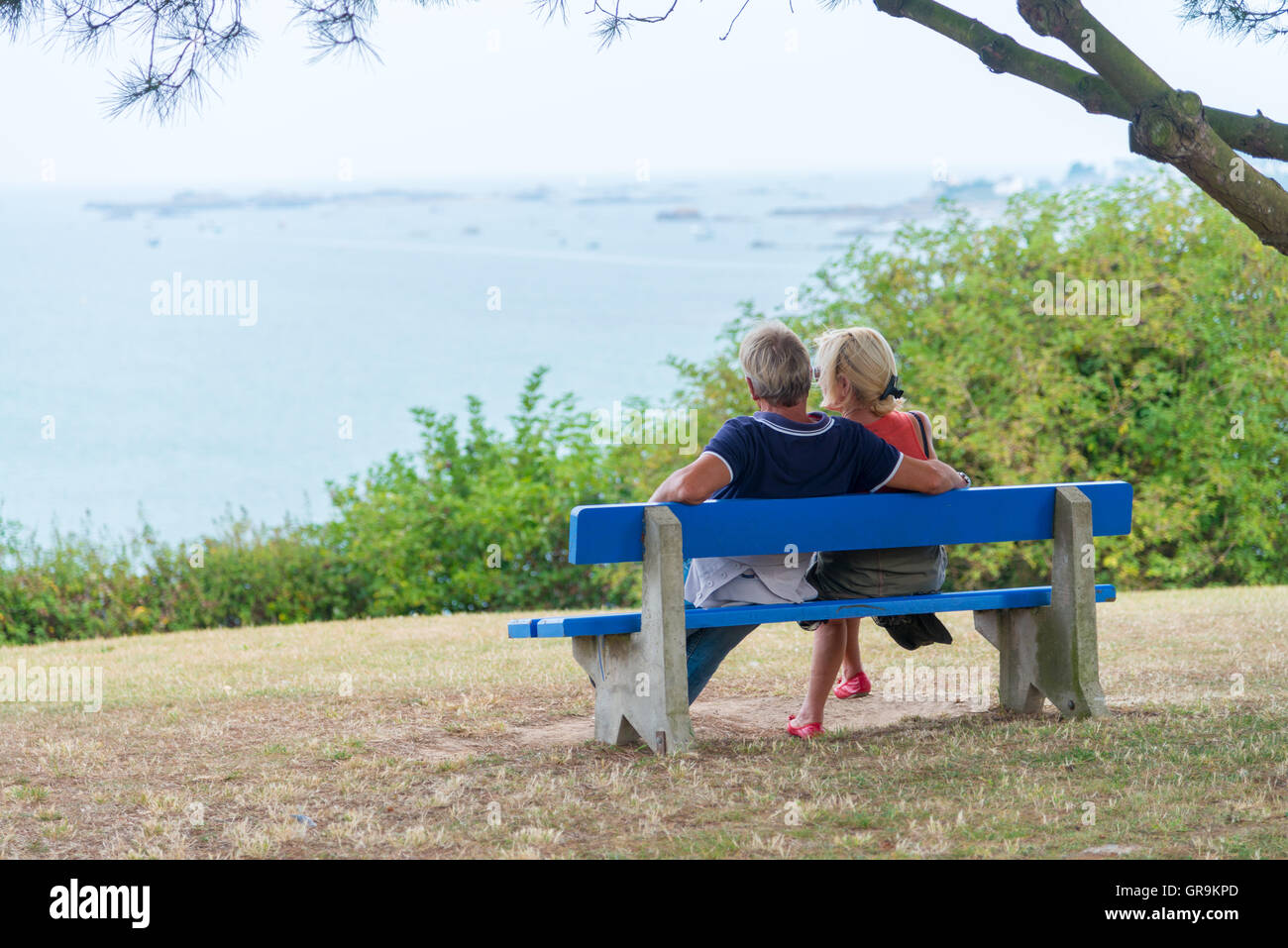 Couple assis sur un banc bleu et regarde la mer Banque D'Images
