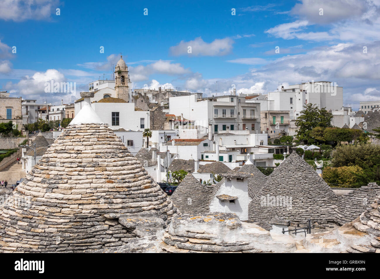 Trulli dans l'avant-plan, l'Église et maisons modernes à l'arrière-plan, Alberobello, Pouilles, Italie Banque D'Images