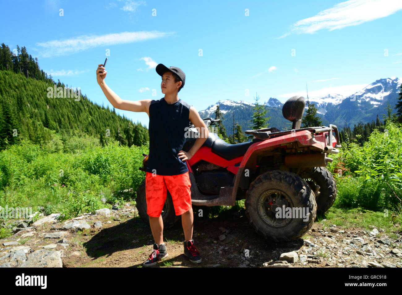GenY homme prend en photo Selfies à côté Nature Valley ATV à l'aide d'iPhone6 Onroute Smartphone via le sentier de gravier près de Whistler, C.-B. Banque D'Images