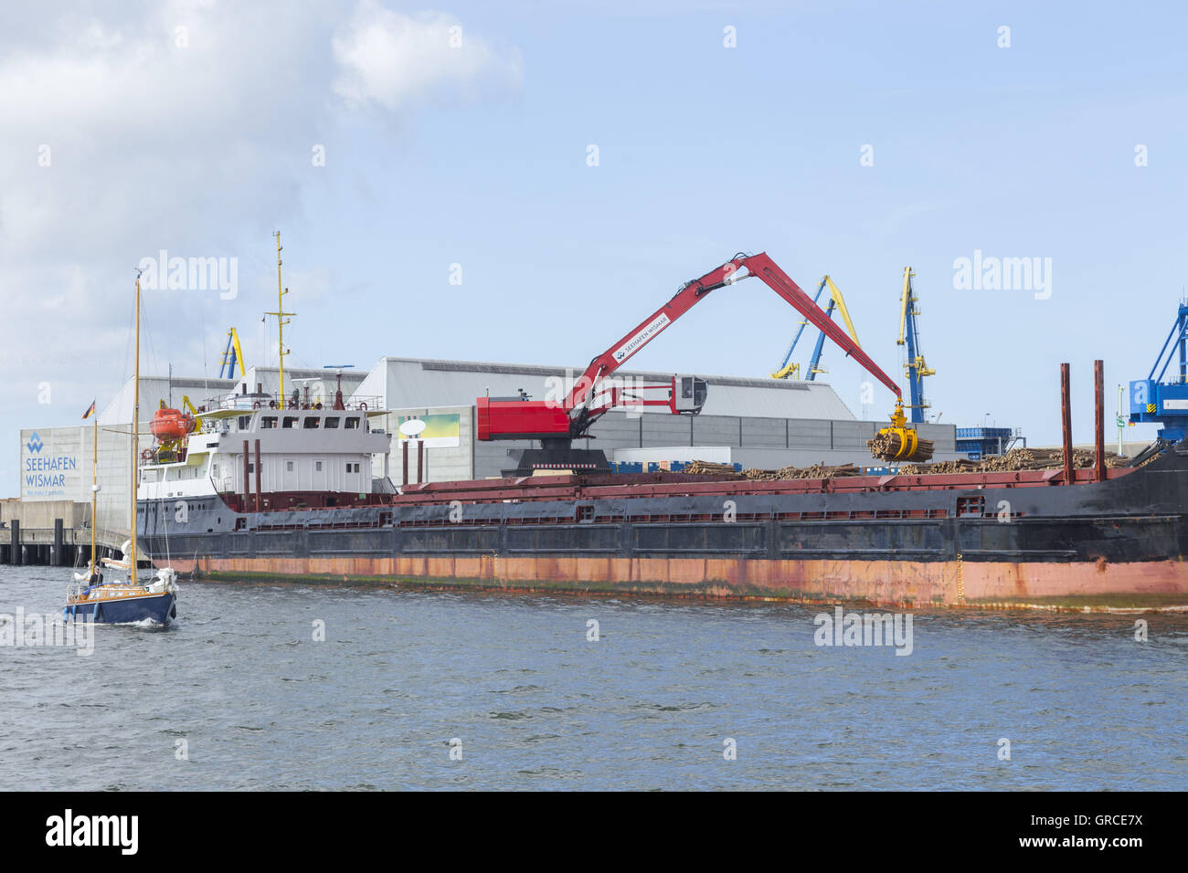 Petit voilier en vertu de moteur d'un cargo dans le port de Wismar Banque D'Images
