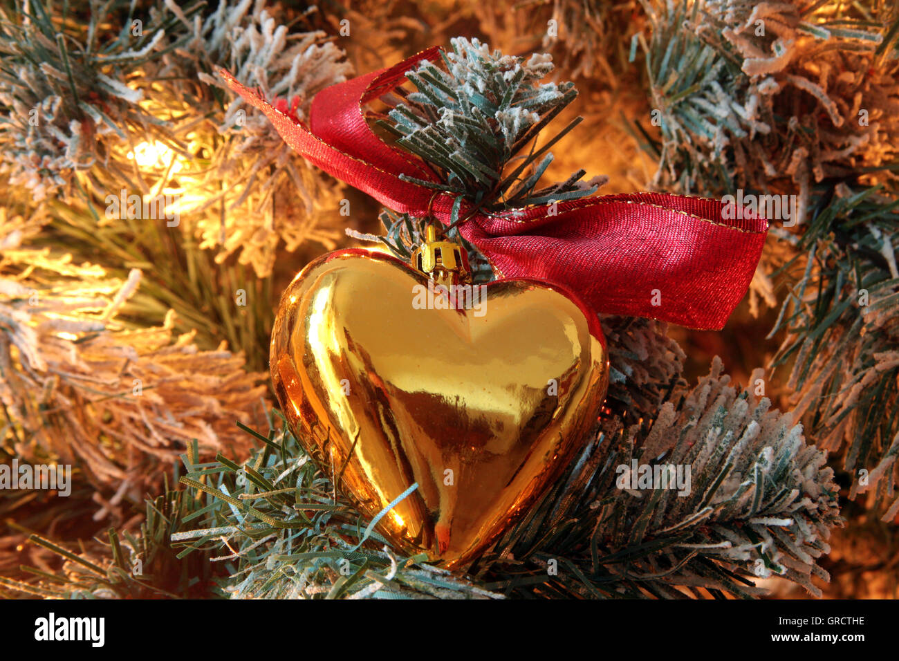 Golden Heart Christmas Tree Ornament avec arc rouge dans un arbre illuminé Banque D'Images